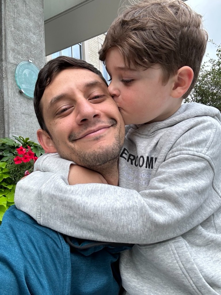 Aziz hugging and kissing his father on the cheek outdoors